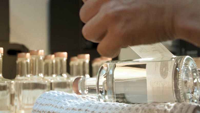 Close-up of a hand sticking a label on a bottle of brandy.