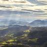 Panoramic view of the Rax Alps with wooded hills and rays of sunshine through clouds.