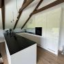 Modern kitchen with white cupboards, black worktop and wooden beams on the ceiling.