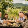 Group of people enjoying a Heurigen snack with wine, a hilly landscape in the background.