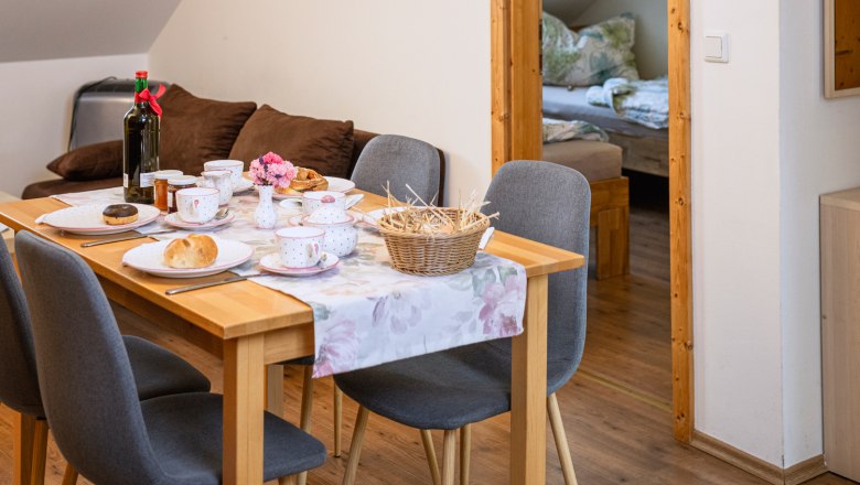 Dining area in a vacation apartment with set table and view into the bedroom.