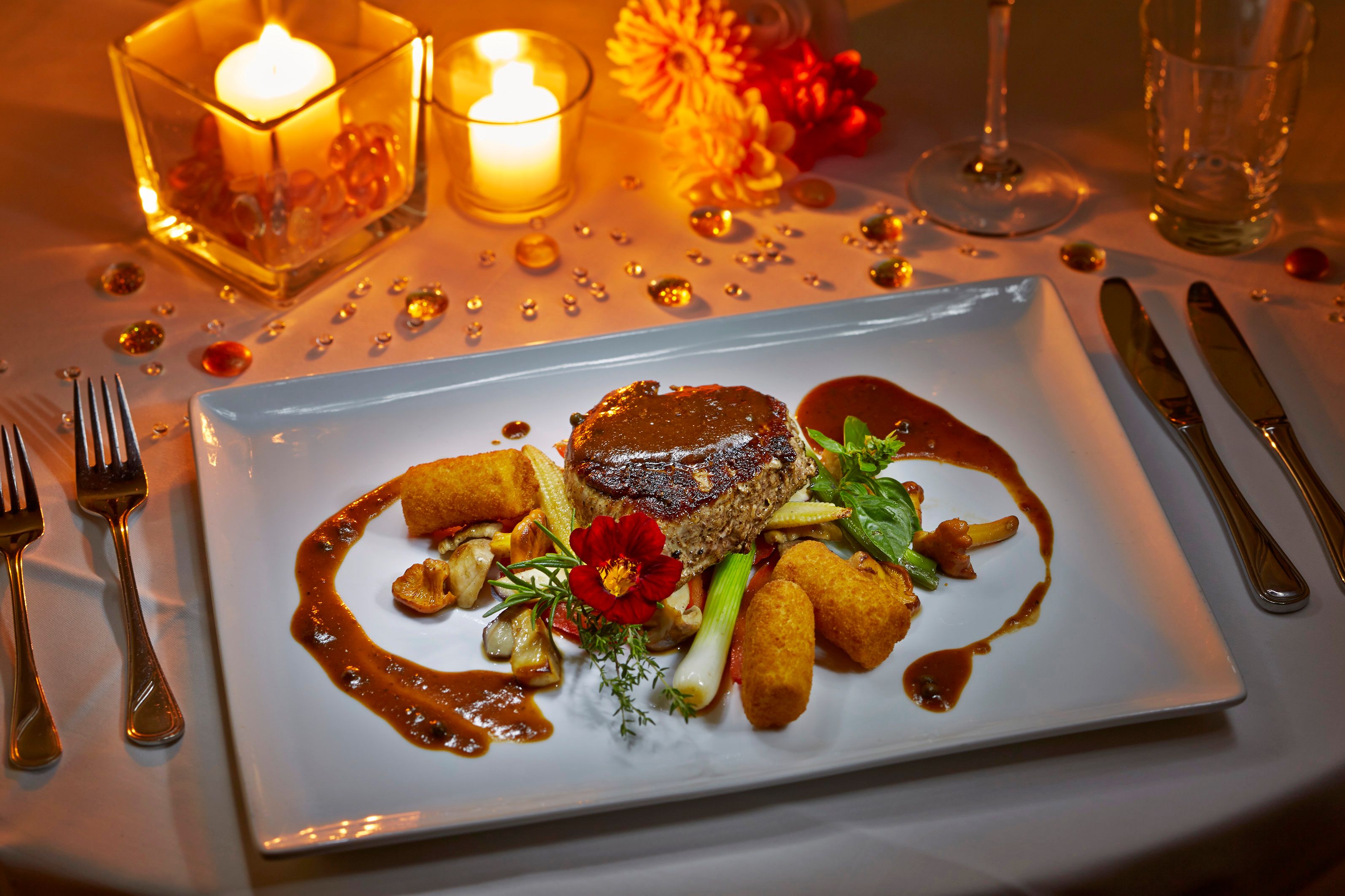 An elegant dish on a white plate, surrounded by candlelight and decorative elements.