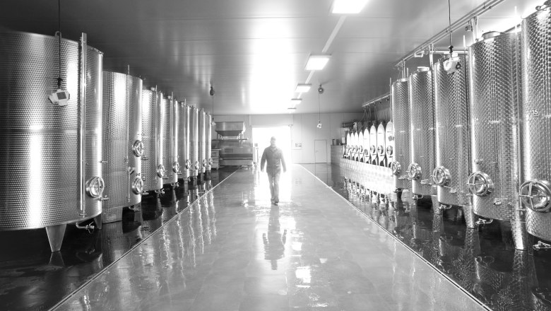 A man walks through a room with large stainless steel tanks.