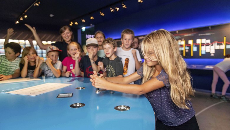 Group of children in a museum, a girl operates a device on a blue table.