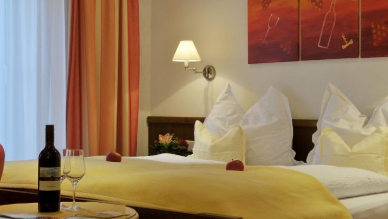 Cozy hotel room with double bed, yellow bedspread, wine bottle and glasses on the table, wall art with wine motif.