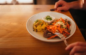 Plate with meat, carrots, potatoes and dip on wooden table.