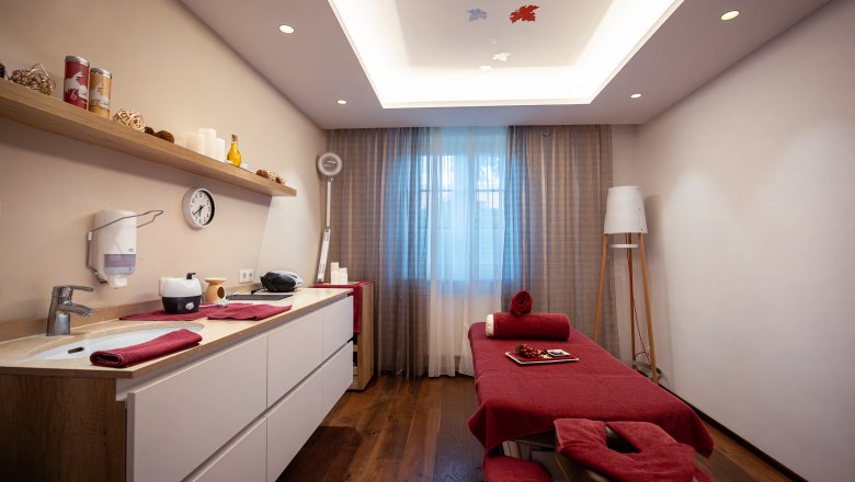 A stylishly furnished spa room with massage table, red towels and decorative elements.