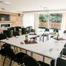 Conference room with U-shaped table arrangement, chairs, wooden wall, TV and large windows with a view of the greenery.