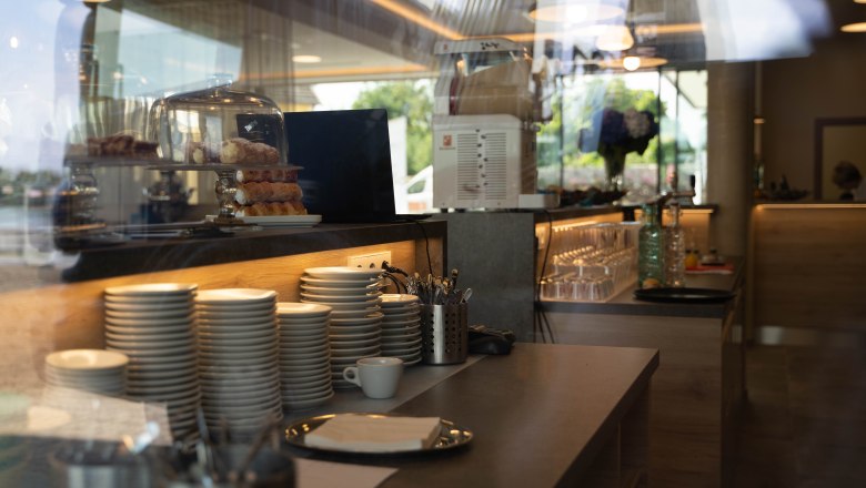 Breakfast counter with stacked plates, cutlery and pastries under a glass bell jar.
