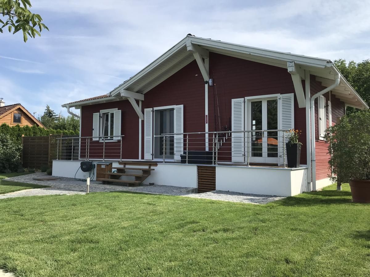 A red wooden house with a white roof and shutters, surrounded by a well-tended garden.