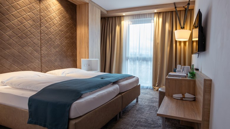 The Alfred, © Niederösterreich Werbung / Maximilian Pawlikowsky Modern hotel room with double bed, wooden paneling and windows with curtains.