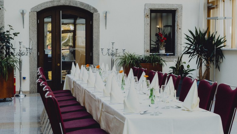 Elegant dining room with table setting, red chairs and plants.