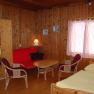 Interior view of a cozy room with wooden walls, red sofa, table, chairs and bed.