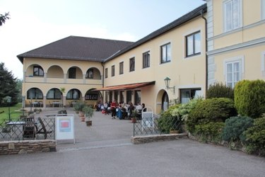 A yellow building with arcades and a terrace where people are sitting.