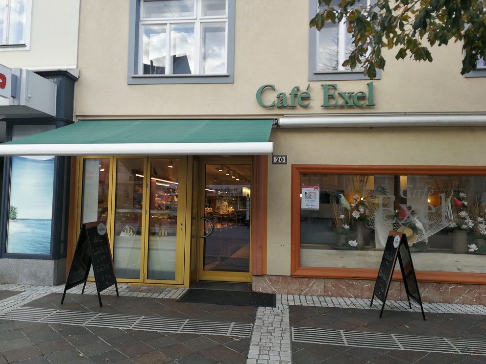 Exterior view of Café Exel with green awning and shop window decoration.