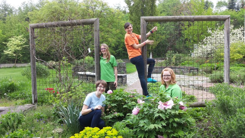 Four people in a garden with flowers and trellises.