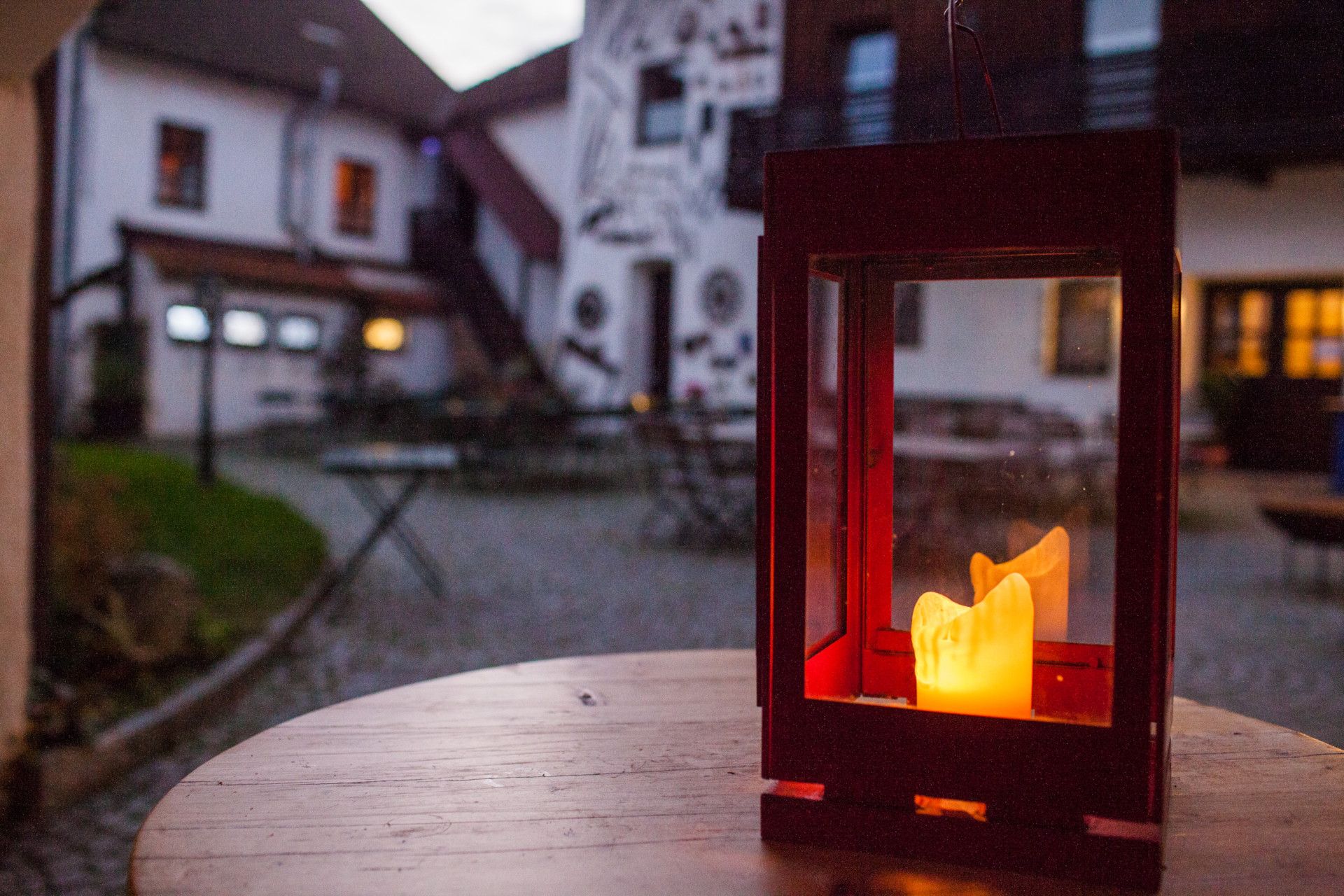 Lantern with a burning candle on a wooden table in the courtyard of a country hotel.