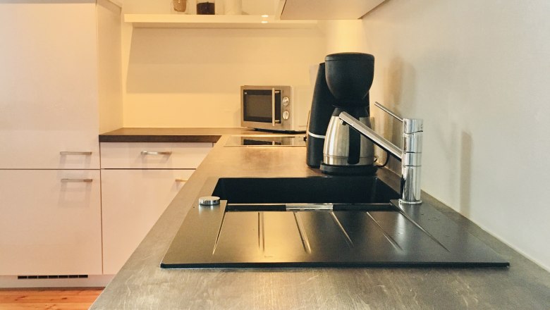 Modern kitchen with wooden worktop, sink, coffee machine and microwave.