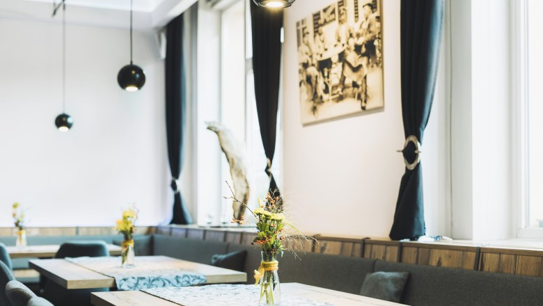 Interior view of a stylish caf&eacute; with wooden tables, flower vases and black curtains.