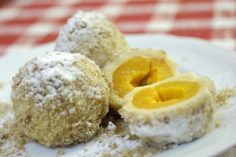 Three apricot dumplings on a plate, one of them sliced