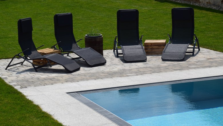Four black sun loungers by the pool on a paved area in the garden.