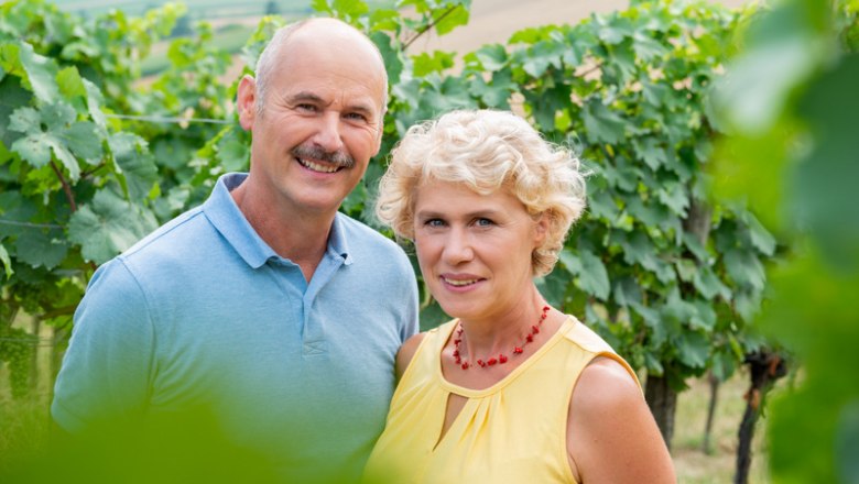 A man and a woman stand smiling in a vineyard.