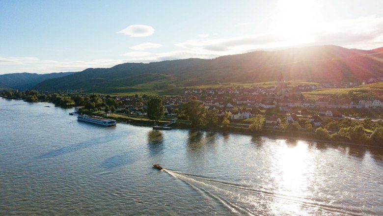 Aerial view of the Wachau with river, boats and village at sunset.