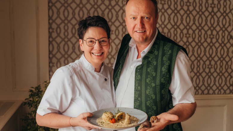 A man and a woman are smiling and holding a plate of food.