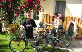 Two people with bicycles in front of a house with flowers and wooden decorations.