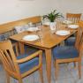 Dining area with wooden table, six covered seats and blue chairs.