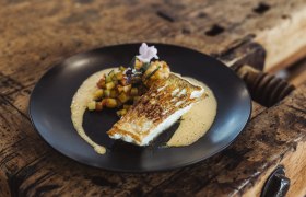 Fried fish with diced vegetables and sauce served on a black plate.