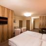 Modern hotel room with double bed, TV, seating area and wooden furniture.