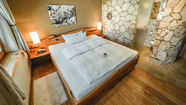 Cozy bedroom with wooden bed, stone walls and modern bathroom.