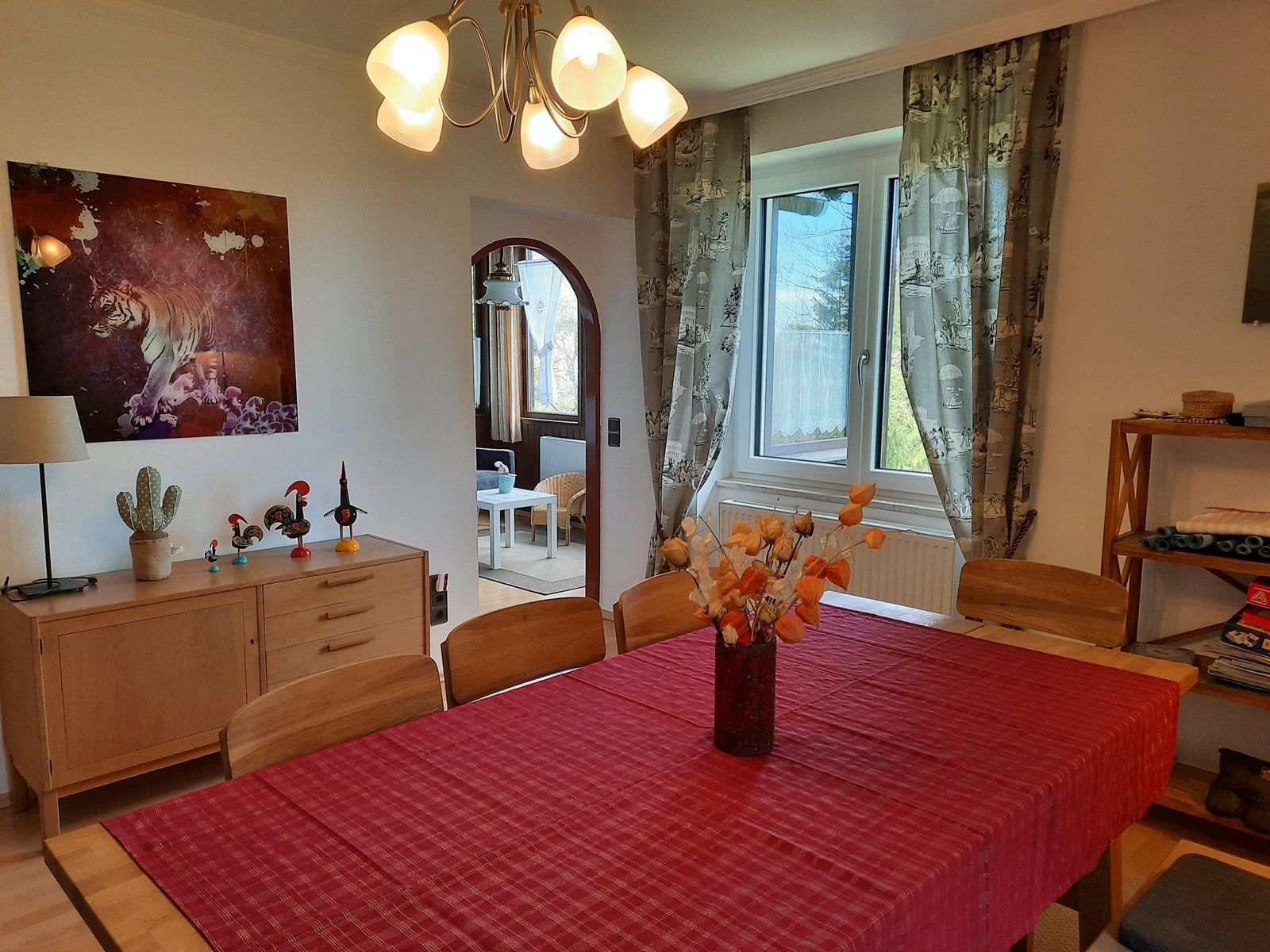 Dining room with red table runner, wooden furniture and tiger picture on the wall.