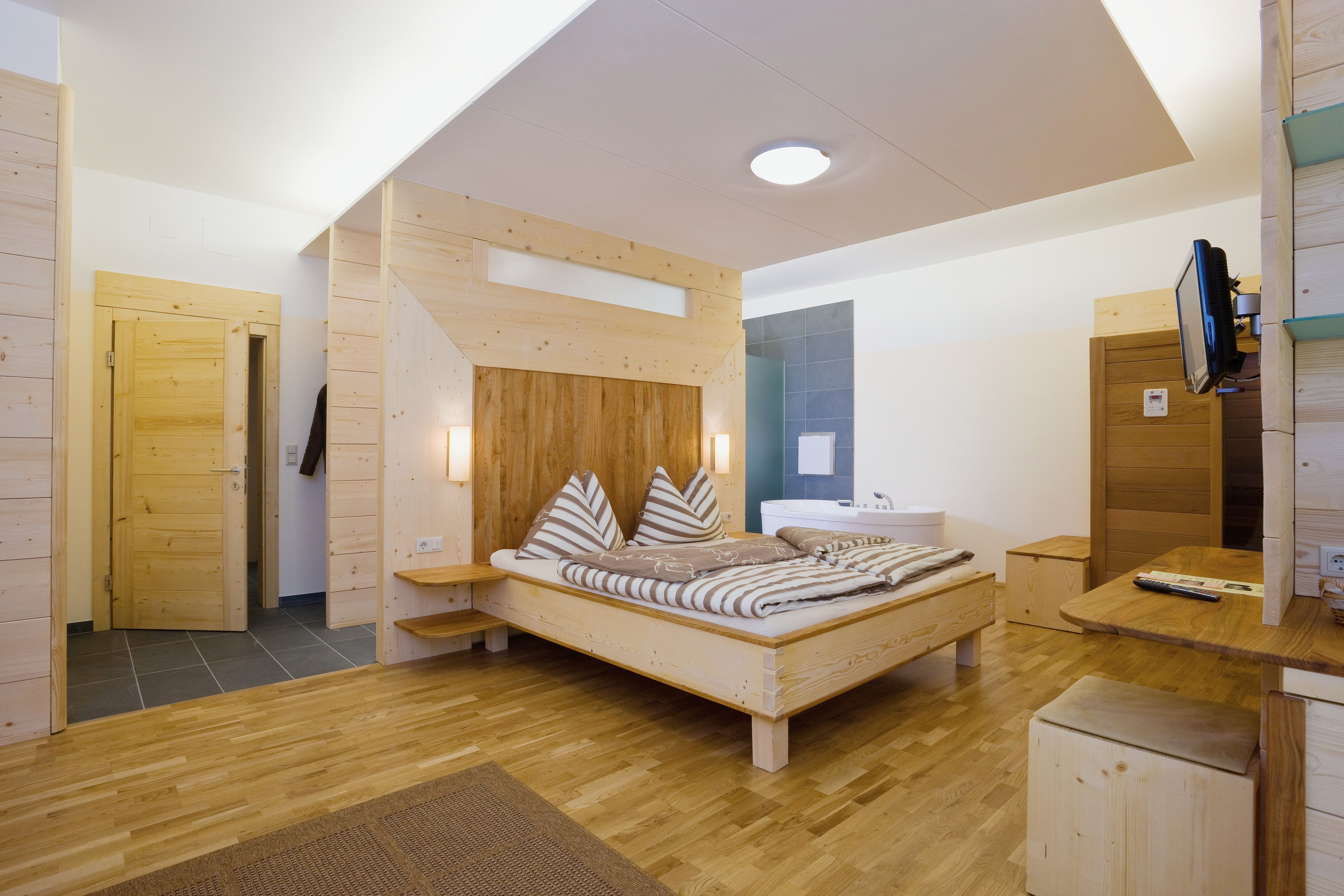 Wooden interior of a modern hotel room with double bed and bathtub.