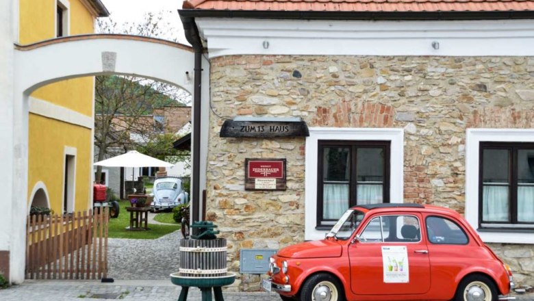 Entrance to a wine tavern with a red vintage car and a yellow building.