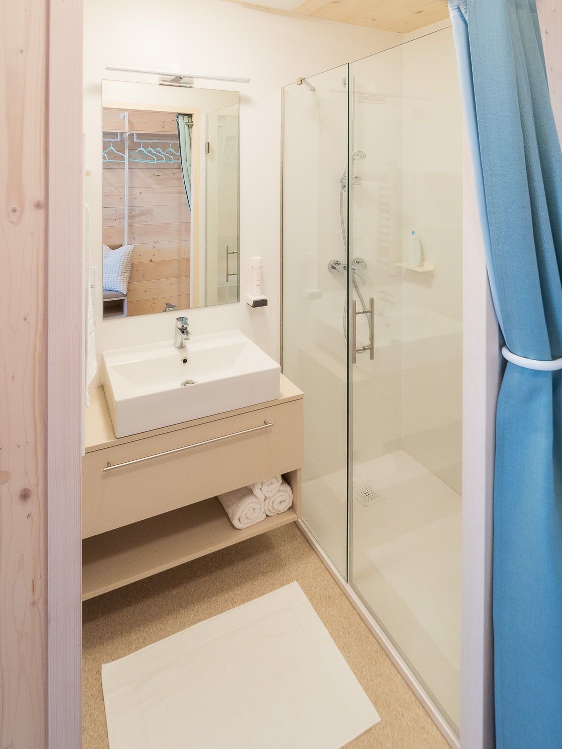 Modern bathroom with washbasin, mirror, shower and blue curtains.