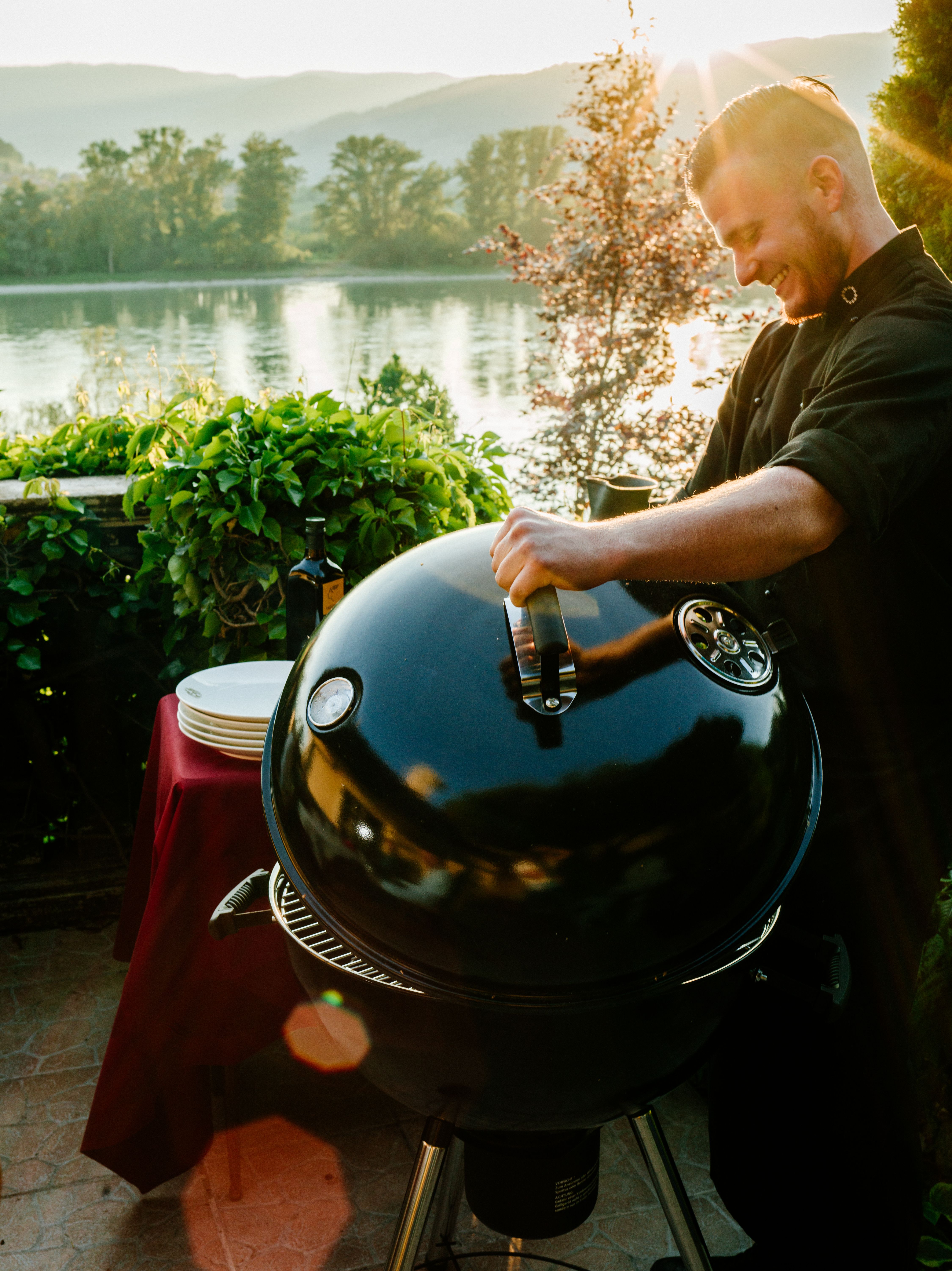 Man barbecuing by the river at sunset.
