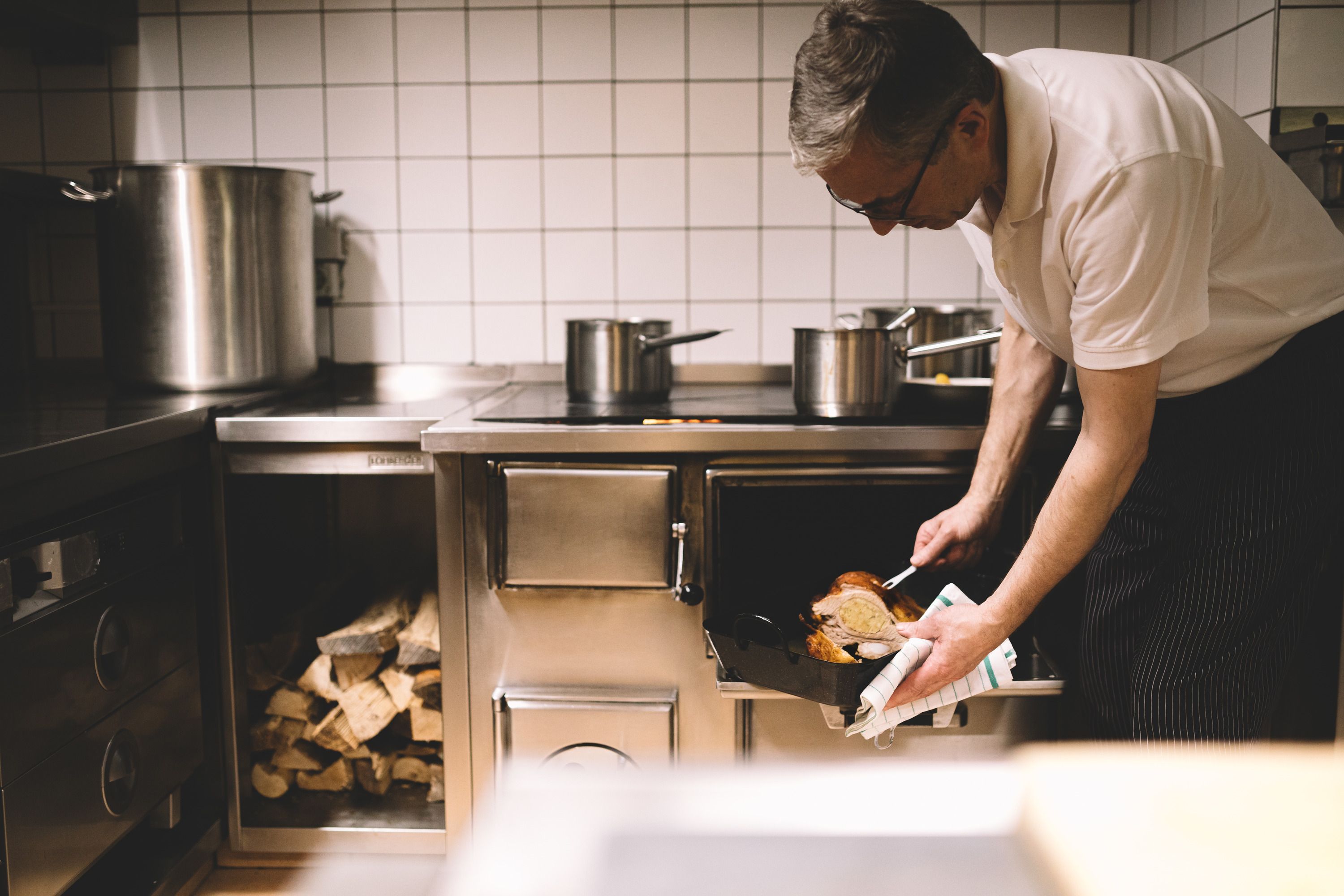 A cook takes a roasted dish out of a wood-fired oven in a restaurant kitchen.