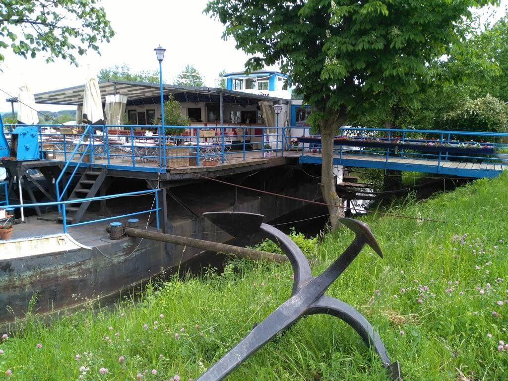 Exterior view of a restaurant on an old ferryboat with blue balustrade and green surroundings.