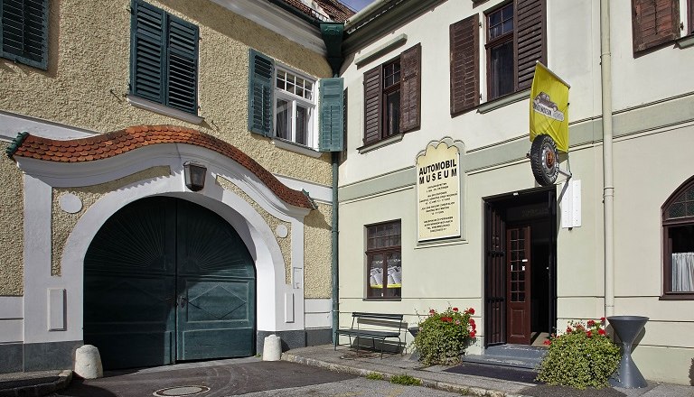 Entrance to an automobile museum with yellow flag and plants.