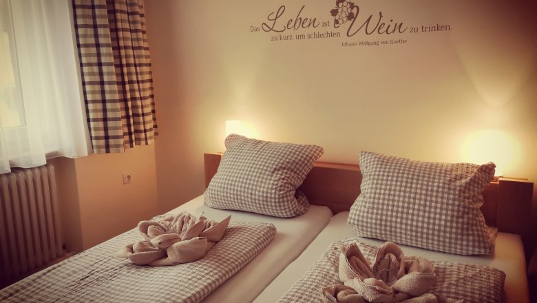 Cozy guest room with two beds, checkered comforters and pillows, decorative towels and a Goethe quote on the wall.