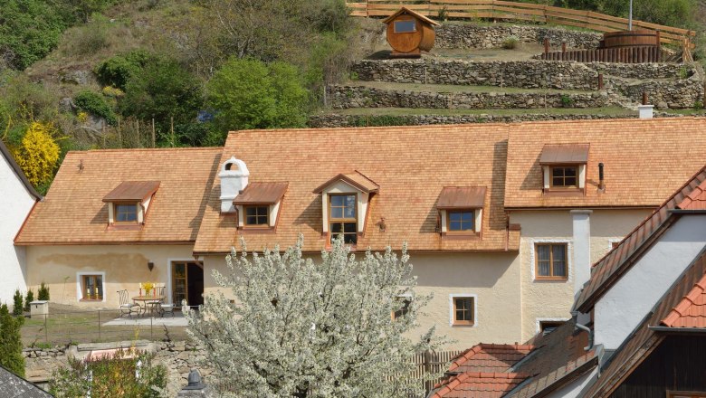 Traditional house with blossoming tree in the foreground, surrounded by green hills.