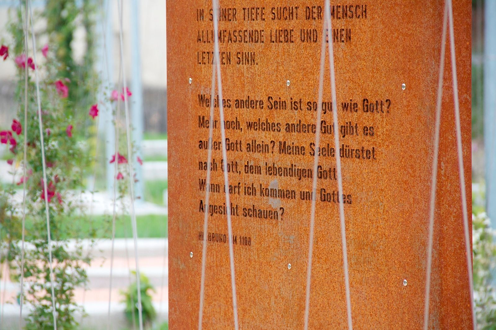 Close-up of a rusty metal plaque with engraved text, surrounded by plants.