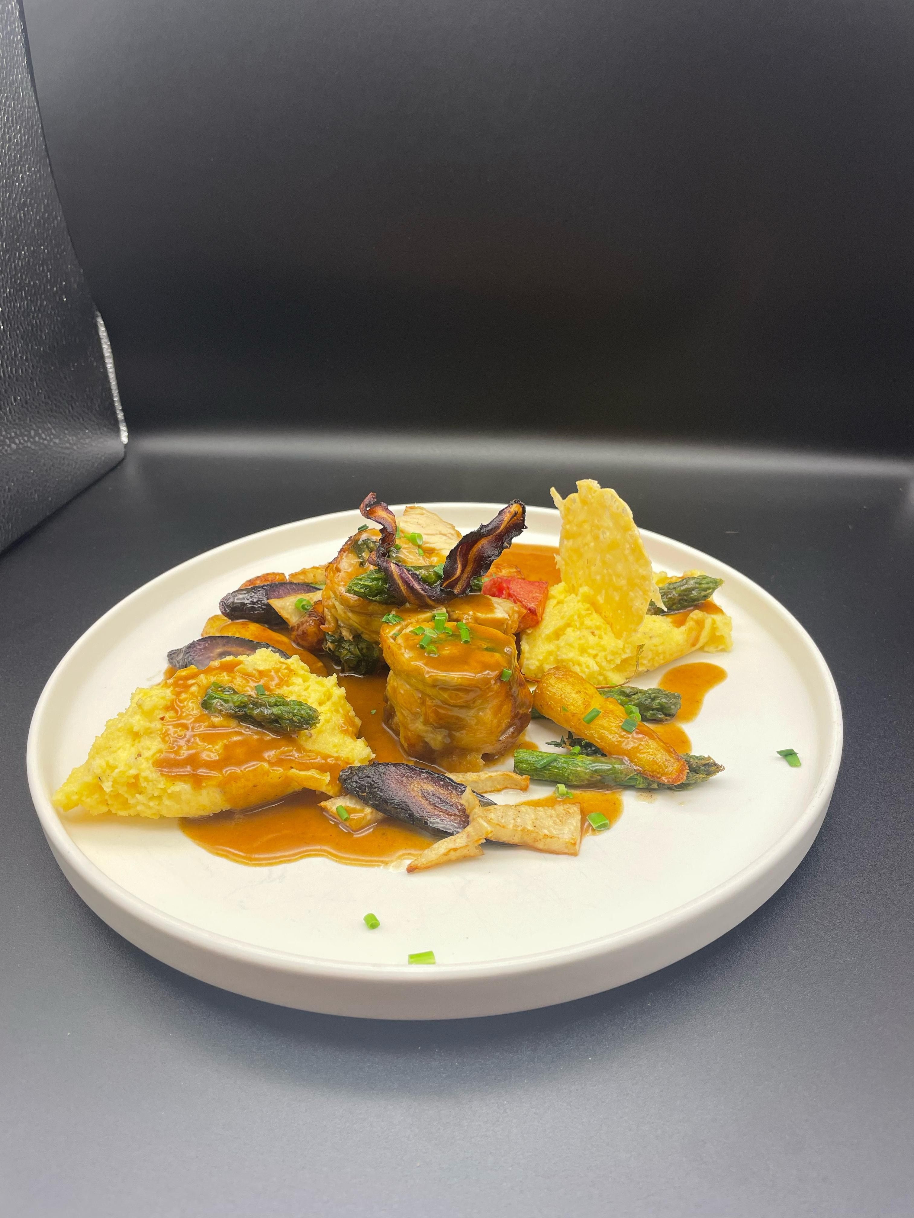 Gourmet dish on a white plate with meat, vegetables and sauce.