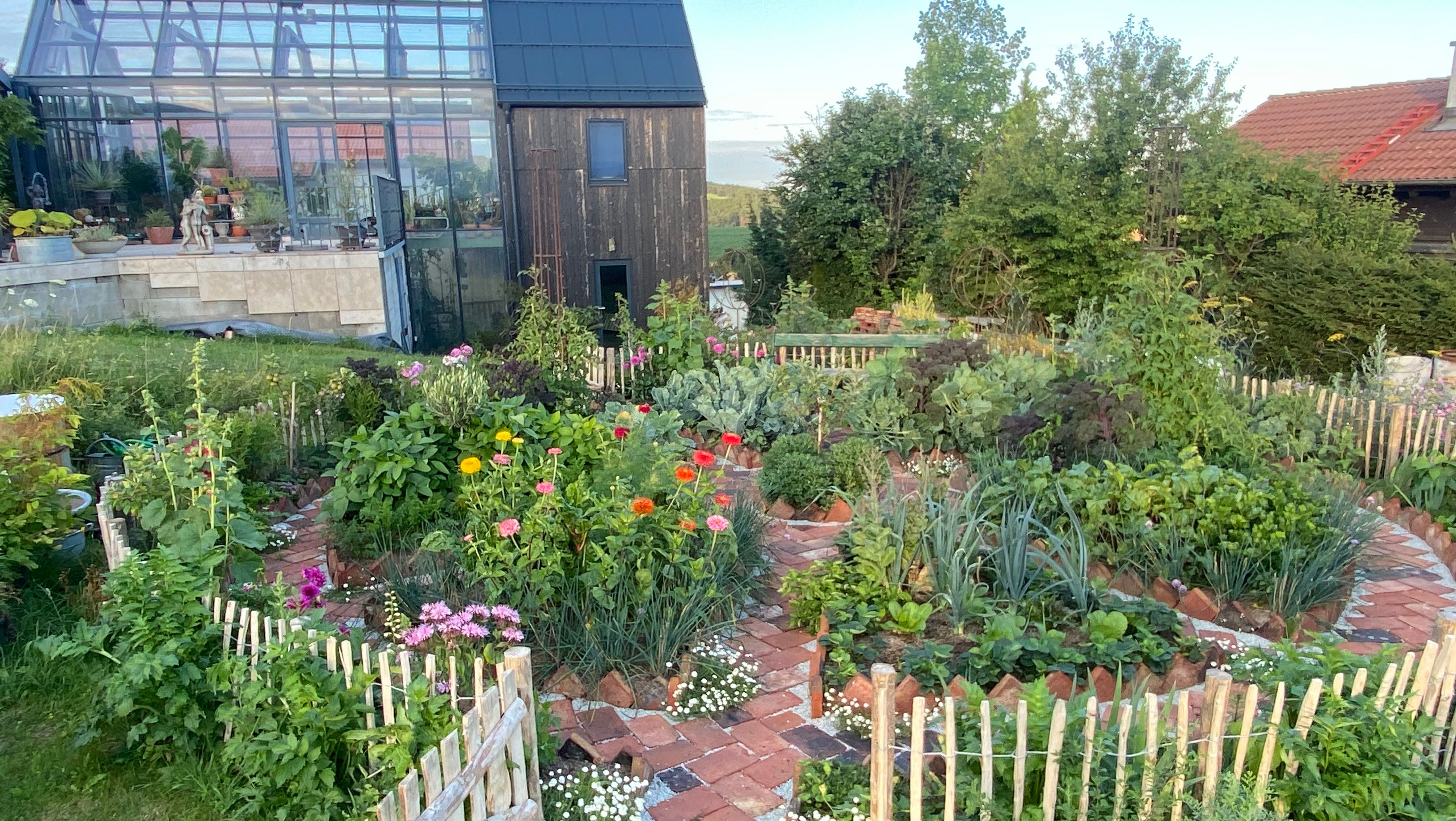 A glass house from the outside in the Ecolution.Lab with a colorful garden in the foreground.
