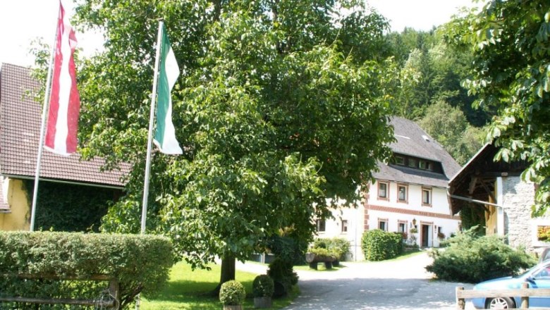 A traditional farmhouse with a garden and flags in the foreground.