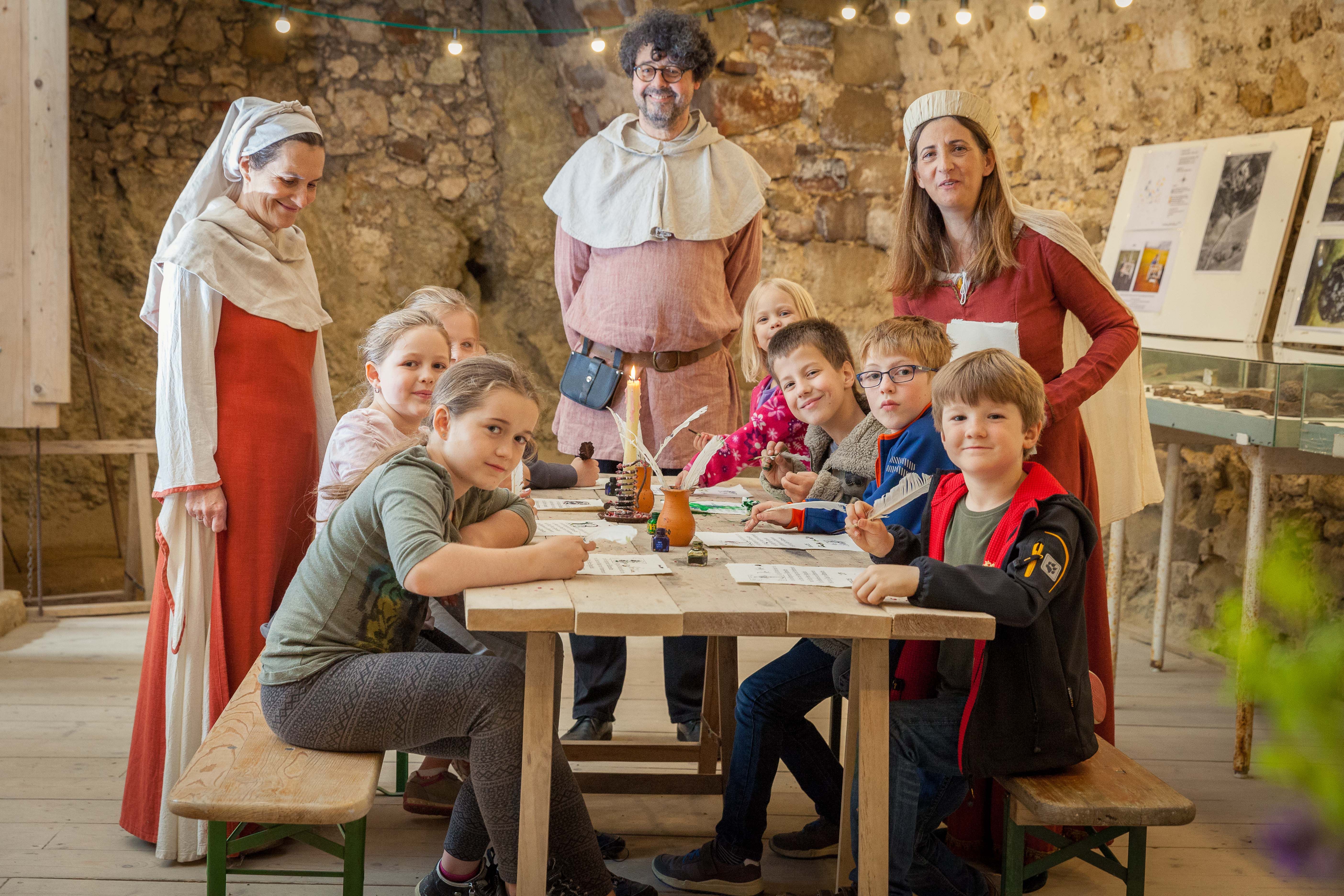 Children and adults in medieval dress at a table in a ruined castle.