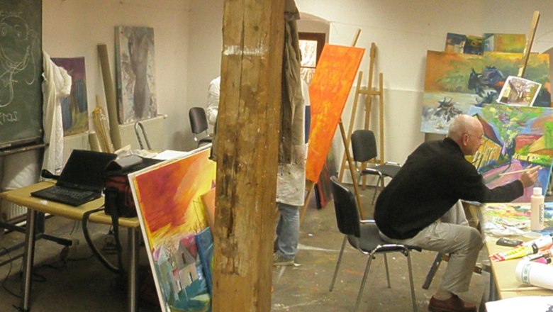 People paint in a studio with easels and colorful paintings.