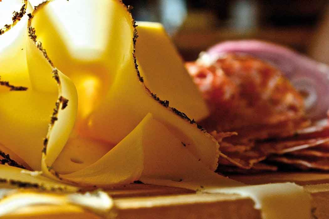 Close-up of thinly sliced cheese and sausage on a wooden board.